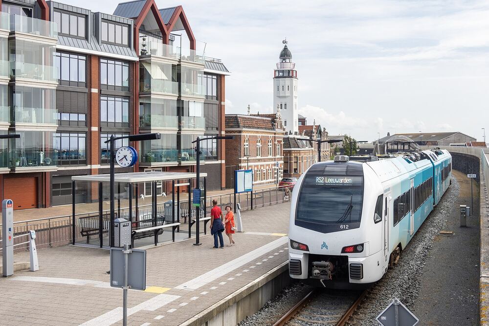 Trein naar Leeuwarden aan het perron van station Harlingen Haven, met de witte vuurtoren van Harlingen op de achtergrond